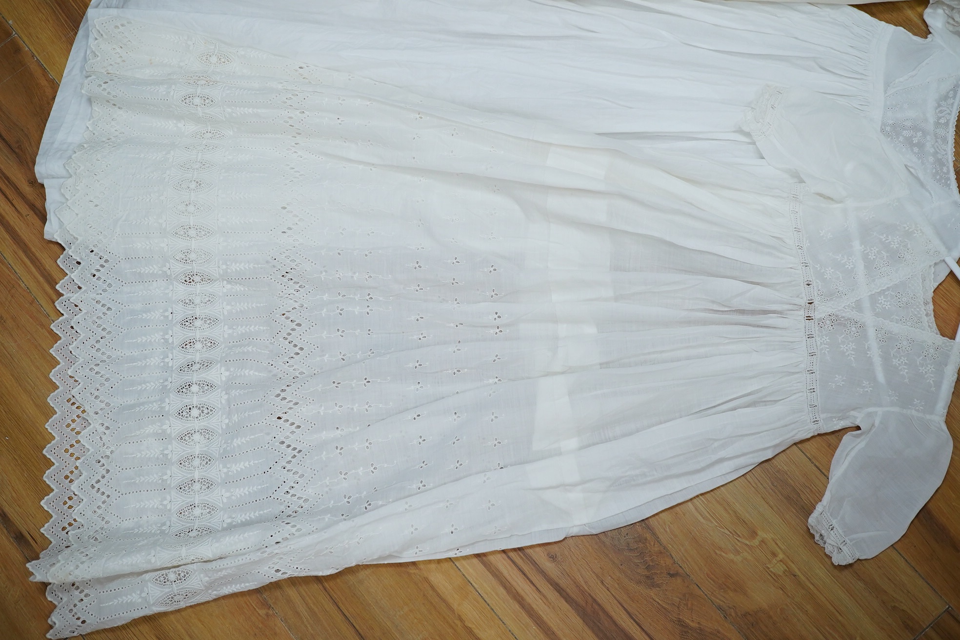 An Edwardian cream silk christening gown, together with four white christening gowns and a baby gown. The silk christening gown edged and inserted with lace and feather stitch embroidery, one Christening gown worked with